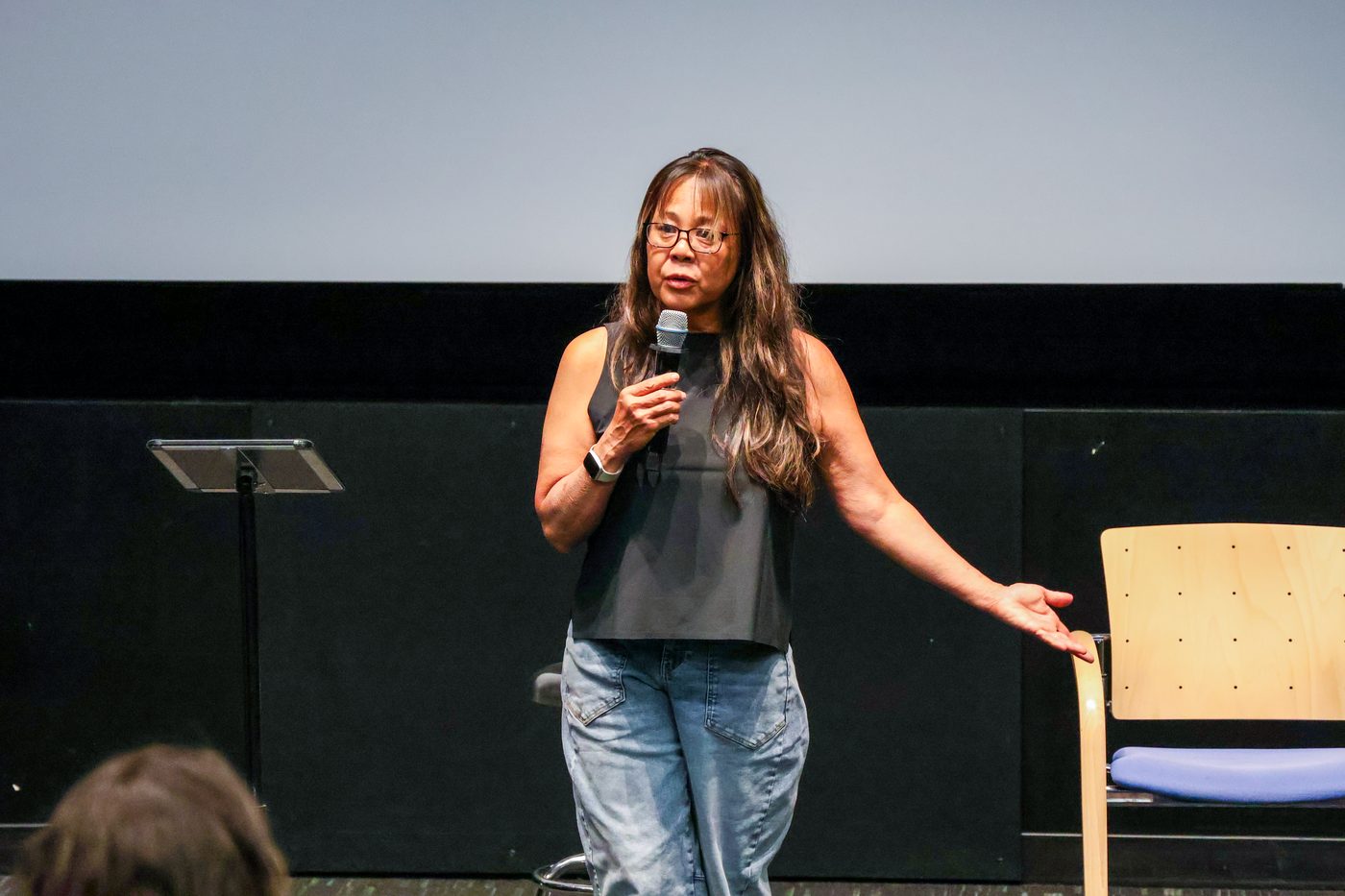 Devaki speaking into a microphone on stage, welcoming the audience
