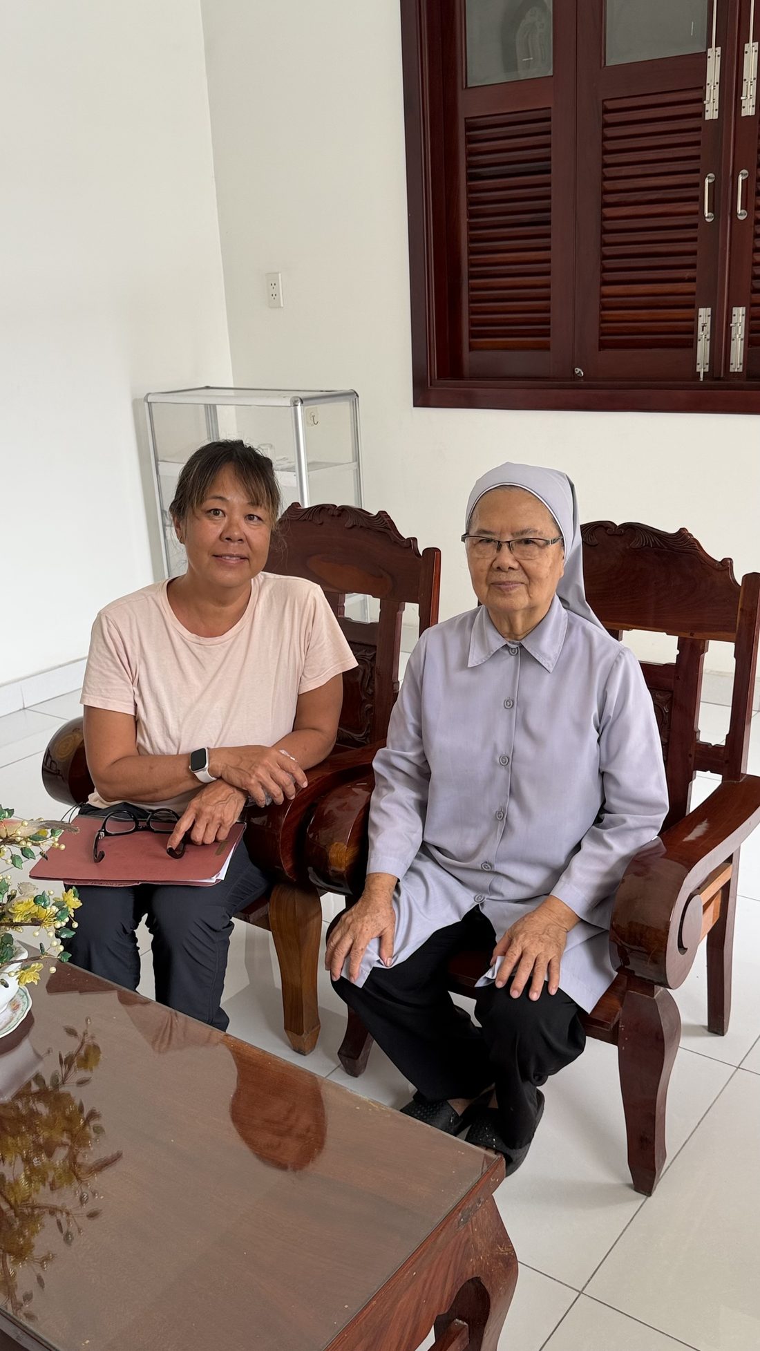 Devaki seated beside an elderly Vietnamese sister during a fieldwork visit